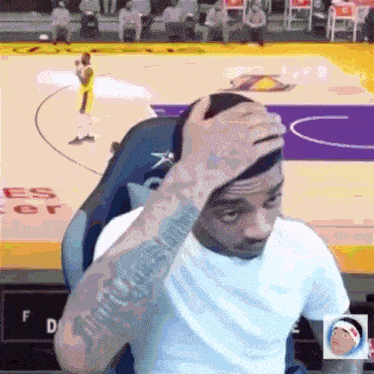a man with a tattoo on his arm is sitting in front of a basketball court