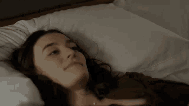 a woman is laying in bed with her head on a pillow and looking at the camera .