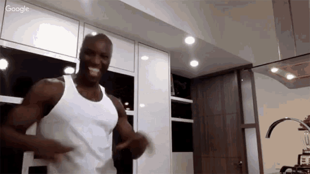 a man in a white tank top is dancing in a kitchen with a google logo on the corner