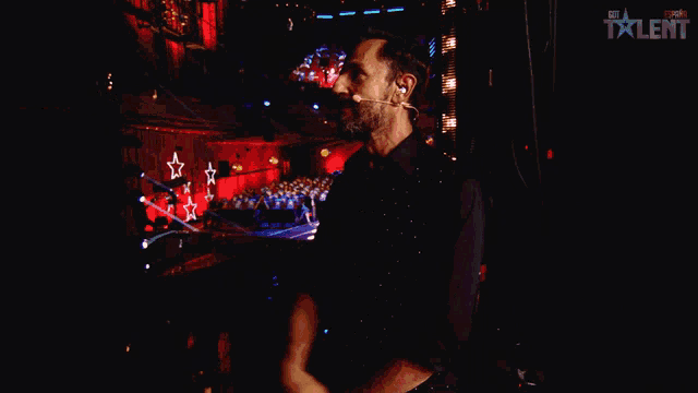 a man in a black shirt stands on a stage with the word talent on the bottom right