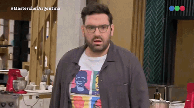 a man with glasses and a t-shirt that says ' coca cola ' on it stands in front of a mixer