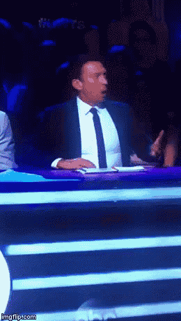 a man in a suit and tie is sitting at a table in front of a blue background