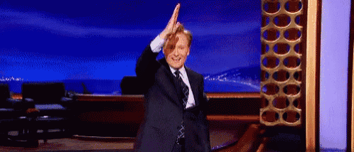 a man in a suit and tie is standing on a stage giving a high five .
