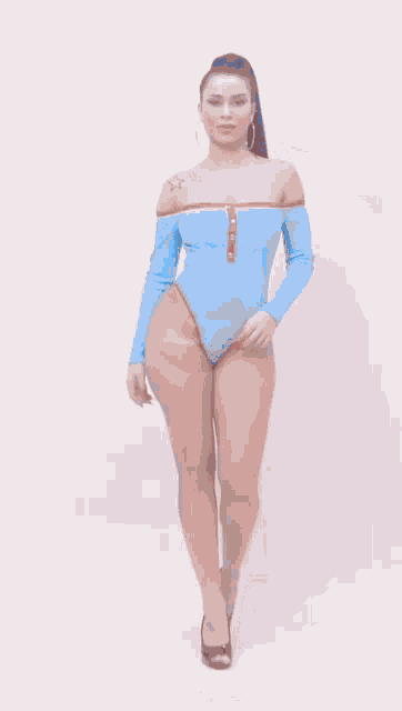 a woman is wearing a blue off the shoulder bodysuit with long sleeves .