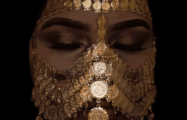 a woman with her eyes closed wearing a gold mask with coins on it