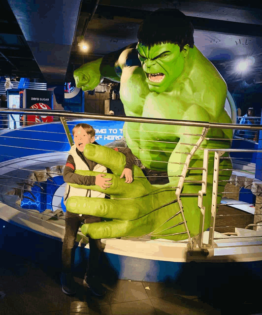 a boy stands in front of a statue of hulk