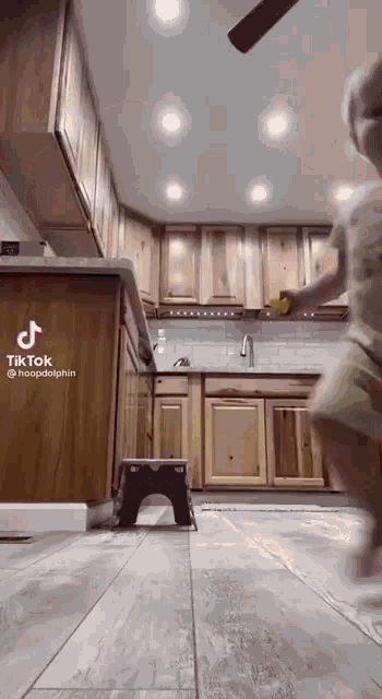 a little girl is playing in a kitchen with wooden cabinets .