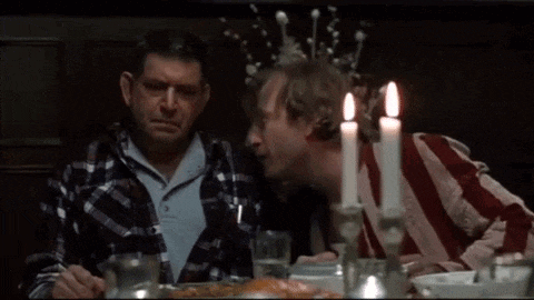 two men are sitting at a table with candles and one is kissing the other on the cheek