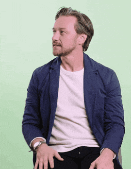 a man with a beard wearing a blue jacket and a white shirt is sitting in a chair .