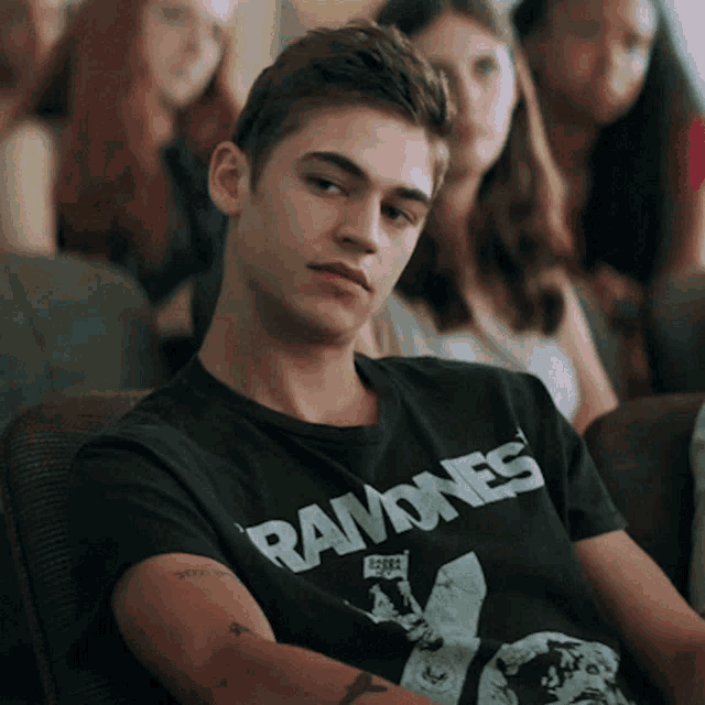 a young man wearing a ramones shirt sits in a chair