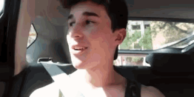 a young man is sitting in the back seat of a car talking .
