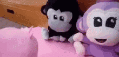 two stuffed monkeys , one black and one purple , are sitting on a pink pillow .