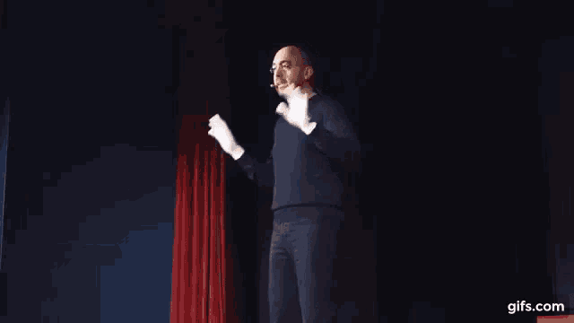 a man wearing white gloves is standing on a stage with his hands outstretched .