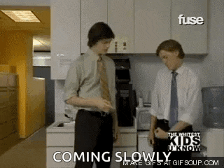 two men in suits and ties are standing in a kitchen with the words coming slowly on the bottom .