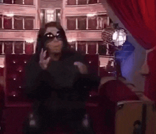 a woman wearing sunglasses is sitting on a red couch in front of a theater .