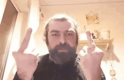a man with a beard is giving the middle finger in a room .