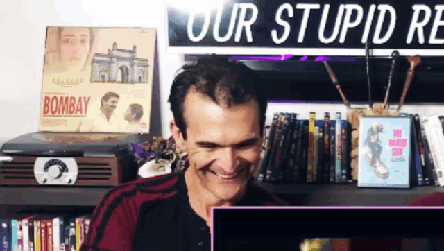 a man is smiling in front of a sign that says " our stupid re "