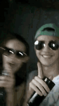 a man and a woman wearing sunglasses and a green hat are holding bottles .