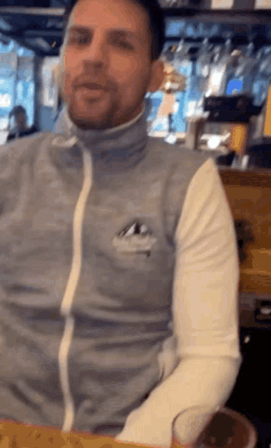 a man sitting at a table wearing a grey vest with a white stripe on the sleeves