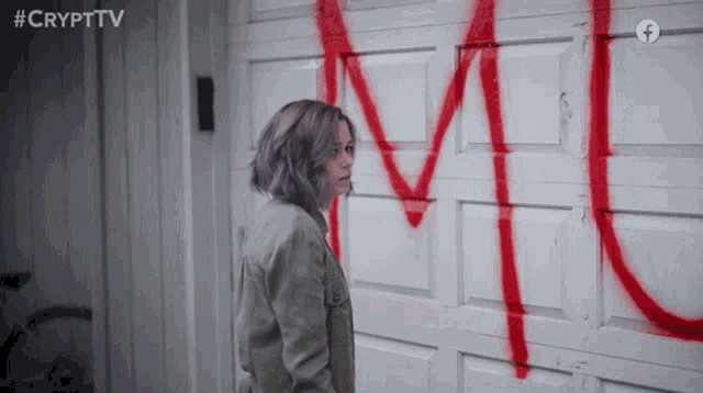 a woman stands in front of a garage door that has the letter m spray painted in red