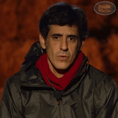 a man wearing a black jacket and a red scarf is standing in front of a sign that says paraiso del paraiso