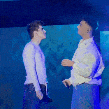 two men standing next to each other in front of a blue wall