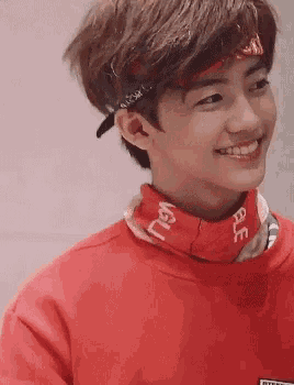 a young man wearing a red sweatshirt and a bandana is smiling .