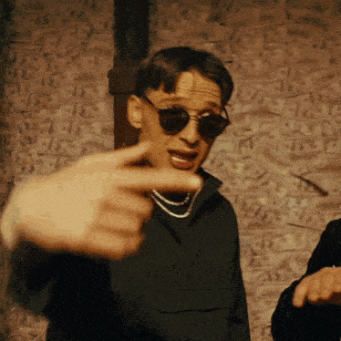 a man wearing sunglasses and a necklace is pointing