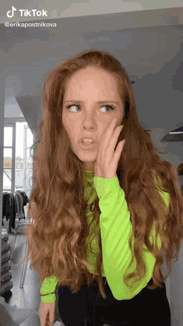 a woman with long red hair is wearing a green shirt and black pants