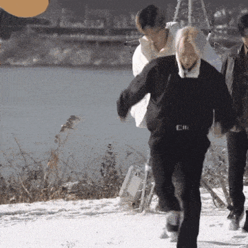 a group of people are walking through the snow near a body of water