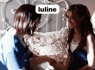two women are sitting on a bed holding hands .