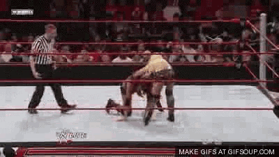 a wrestler is laying on the ground in a wrestling ring while a referee walks around .