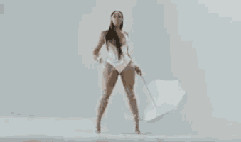 a woman in a white swimsuit is holding an umbrella and dancing .