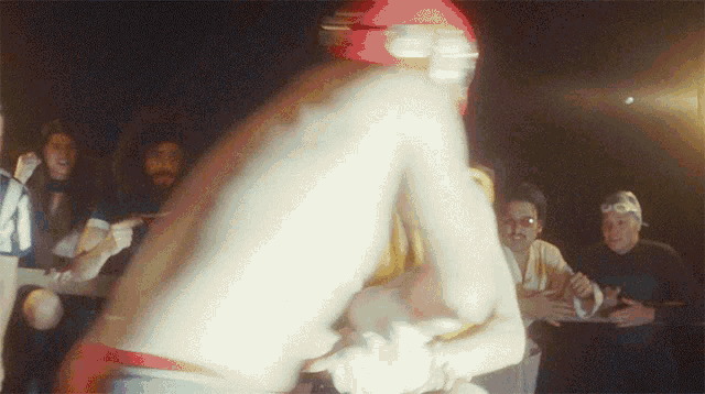 a shirtless man in a red helmet stands in a crowd