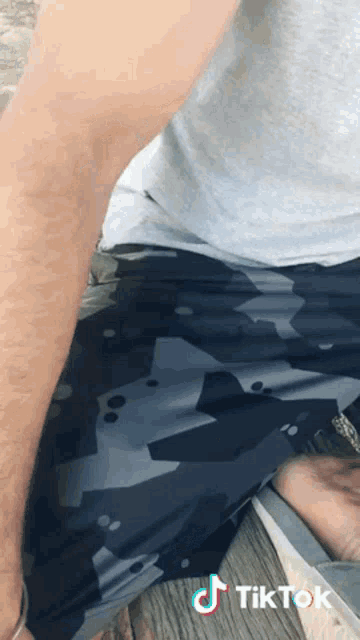 a man wearing camouflage shorts and a grey shirt is kneeling down on a wooden surface .