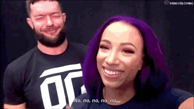 a woman with purple hair is smiling while a man with a beard looks at her .