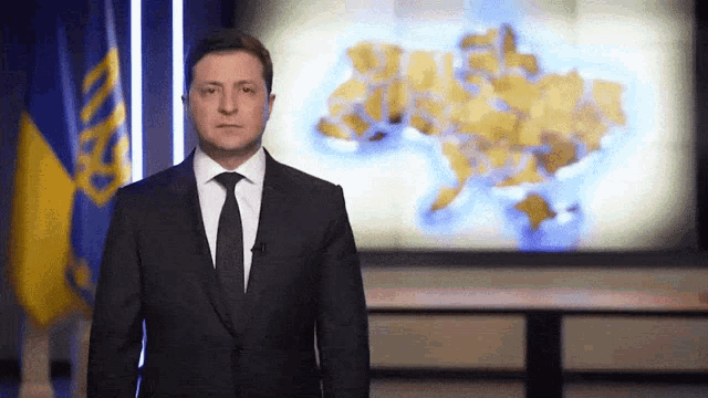 a man in a suit and tie stands in front of a large map