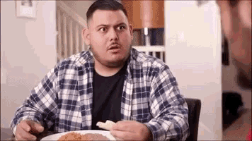 a man in a plaid shirt is sitting at a table eating a meal .