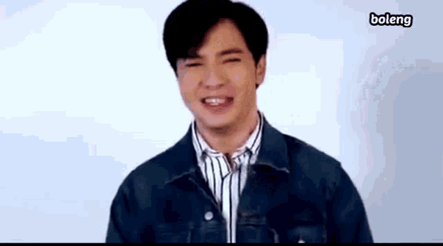 a young man wearing a denim jacket and striped shirt is smiling .