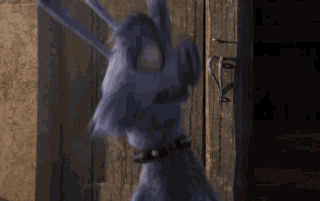 a blue furry animal with a black collar is standing in front of a wooden door