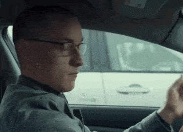 a man wearing glasses is driving a car with a sticker on the windshield that says airbag