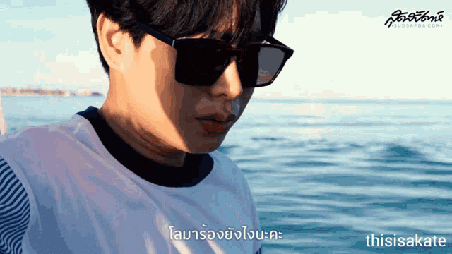 a man wearing sunglasses and a white shirt is standing in front of a body of water