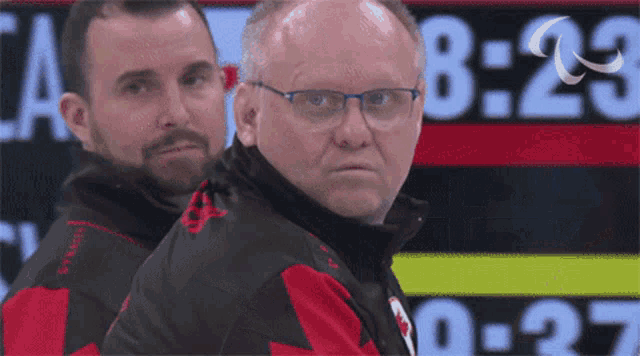 a man wearing glasses stands in front of a scoreboard that says 8:29
