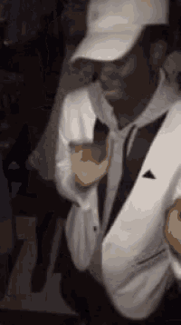 a man in a white suit and hat is dancing in a club .