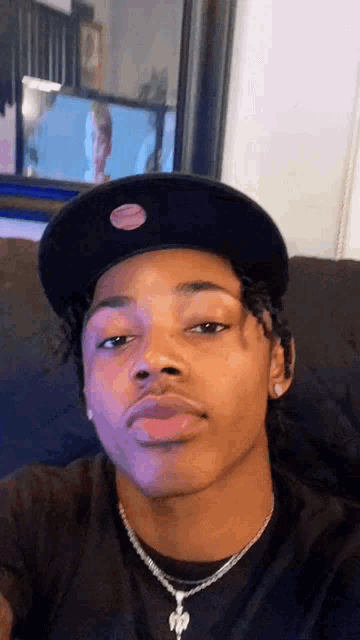 a young man wearing a black hat and a necklace is sitting on a couch .
