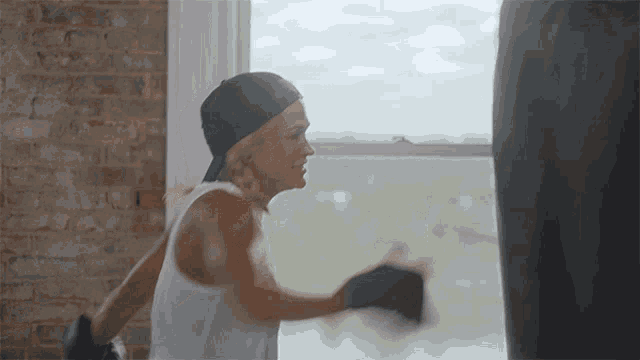 a woman wearing boxing gloves is punching a punching bag in front of a window