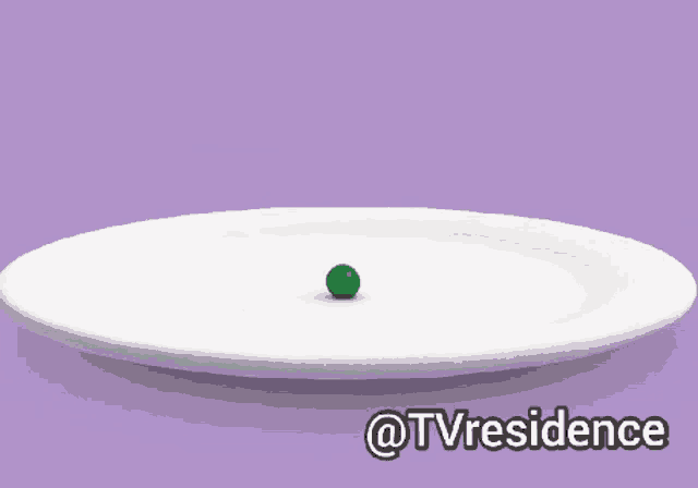 an orange fork is reaching for a green ball on a plate