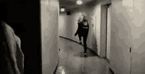 a black and white photo of a man walking down a hallway .