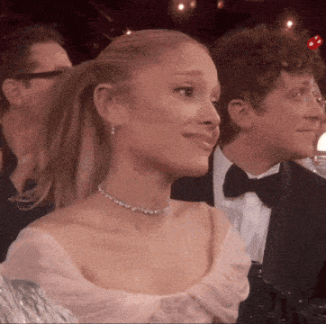 a woman in a ponytail is sitting in a crowd with a man in a tuxedo .