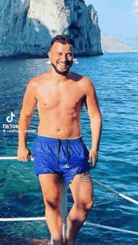 a shirtless man in blue swim trunks is standing on a boat in the water .
